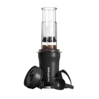 Zdjęcie AeroPress Go Plus w kolorze czarnym, prezentujące pełny zestaw do parzenia kawy, w tym prasa AeroPress, czarna miarka, pokrywka oraz pojemnik do przechowywania. Zestaw przeznaczony do łatwego przygotowywania kawy w podróży.